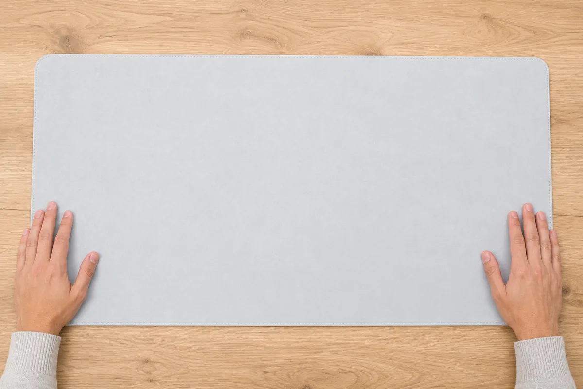 Vue du dessus de deux mains venant de positionner un grand sous-main gris clair au centre d'un bureau vide, parallèle au bord avant